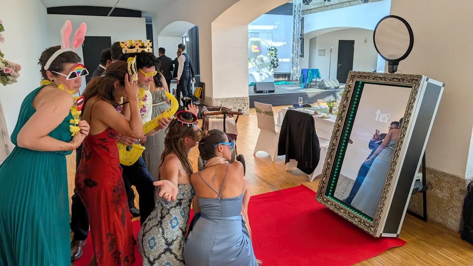 Gäste mit bunten Requisiten posieren gemeinsam vor dem Fotospiegel auf dem roten Teppich.